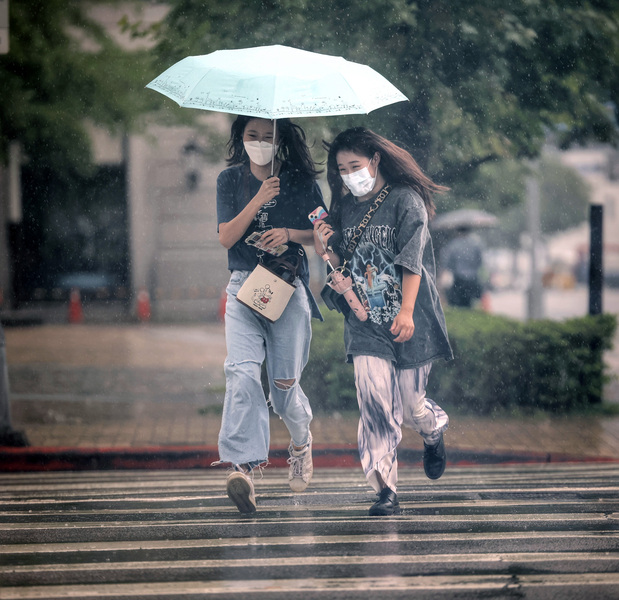 圖為台北大直街頭民眾雨中共撐一傘,快跑過馬路。(中央社)