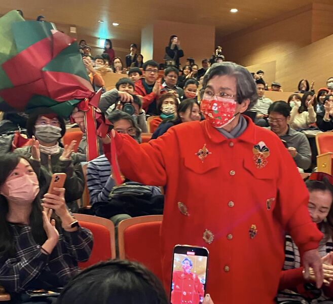 89歲的李金里一身紅衣衫,學生劉孟捷的孜矻努力與成就,讓她喜形於色,尤其接到學生感恩花束,她開心不已。(作者提供)